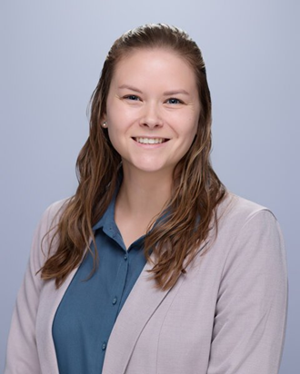 Portrait of a smiling woman with long brown hair, wearing a blue blouse and light cardigan against a light blue background.